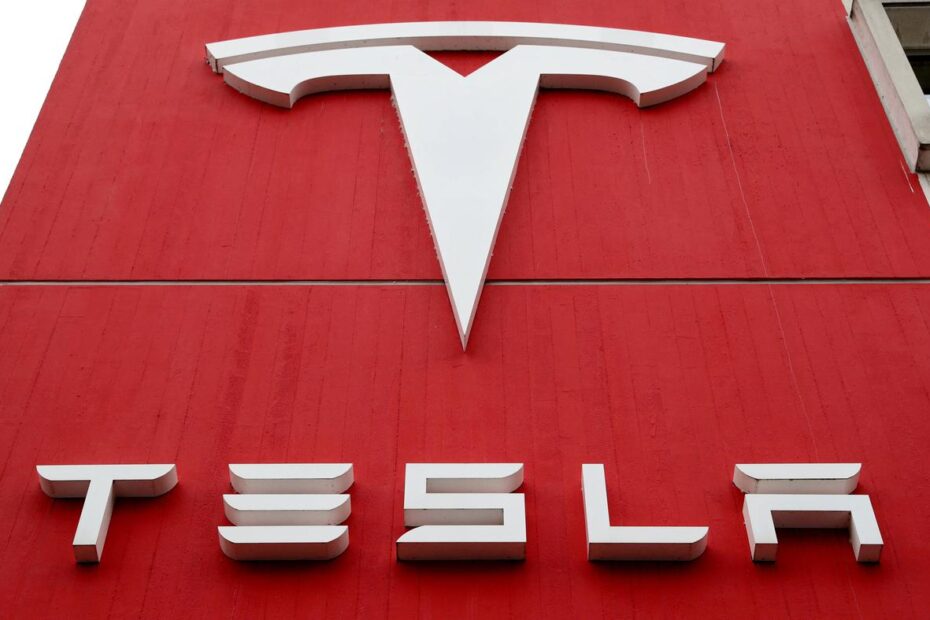 Logotipo branco da Tesla com símbolo T estilizado e nome da empresa em parede vermelha