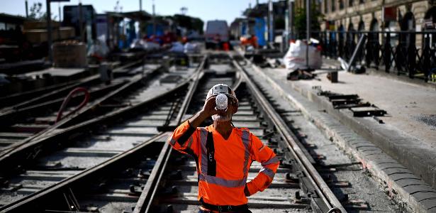Trabalhador bebe água para se refrescar enquanto trabalha em um canteiro de obras de linhas de bonde durante uma onda de calor em Bordeaux, sudoeste da França