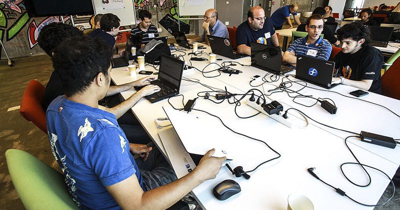 Jovens sentados em volta de uma mesa trabalhando em laptops