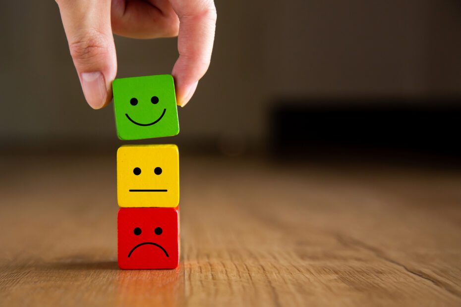 Uma pessoa colocando um cubo com carinha verde em cima de uma pilha com carinha vermelha e amarela; satisfação do cliente