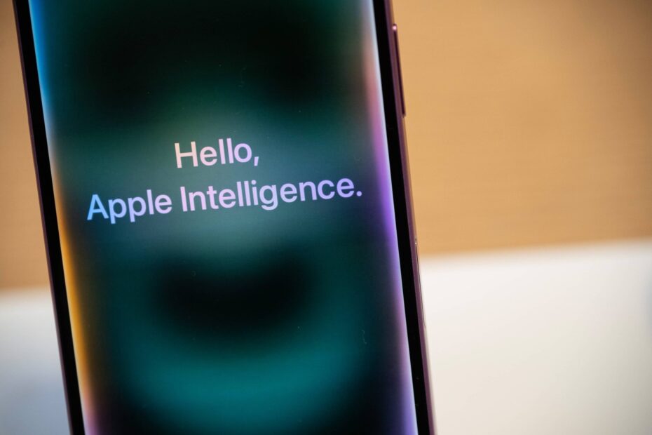 Celular com texto 'Hello, Apple Intelligence' na tela, sobre fundo turvo.